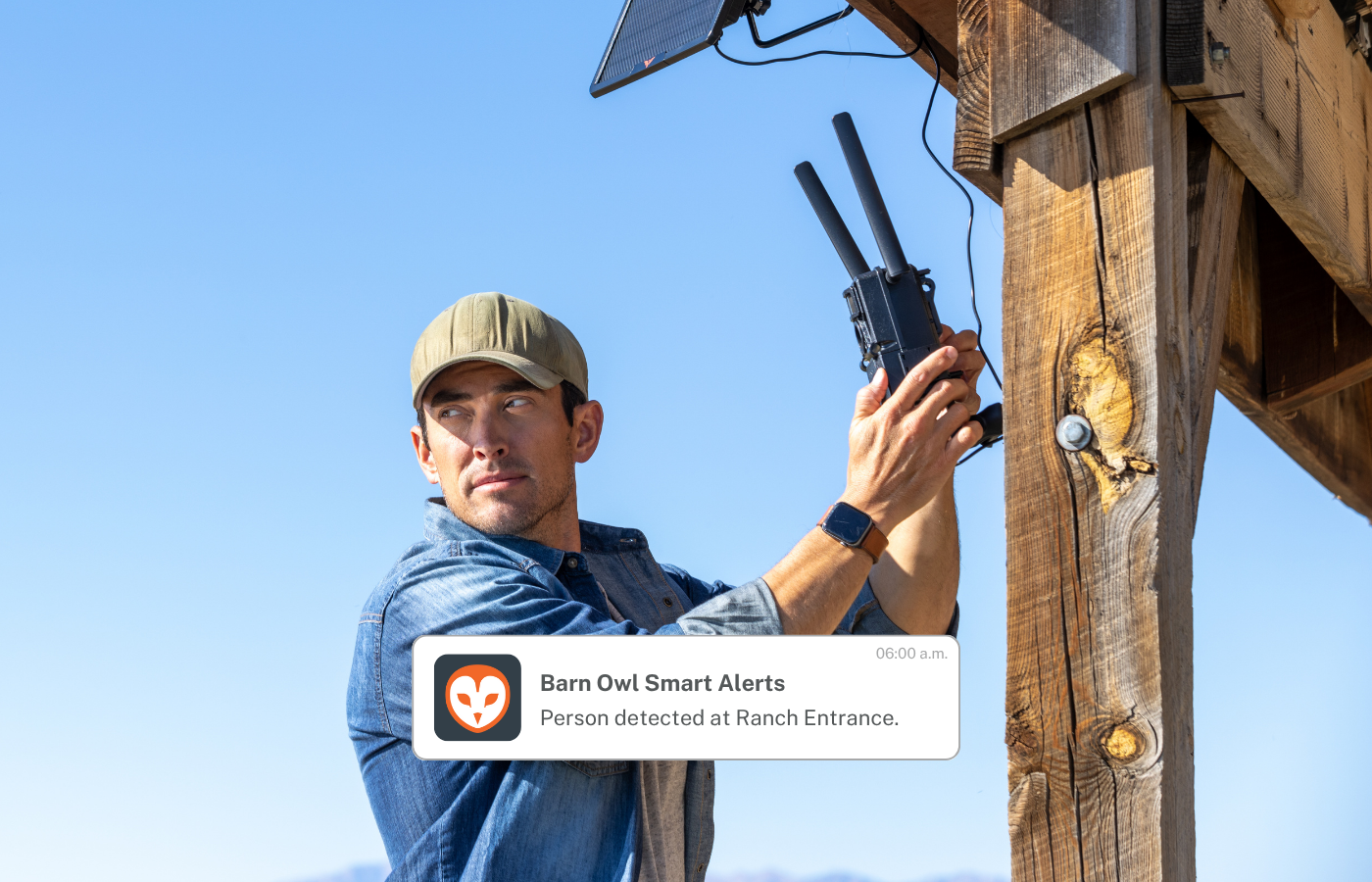 Man holding a device with Barn Owl Smart Alerts on a wooden post against a blue sky.